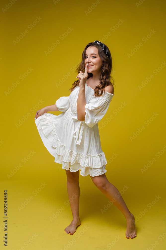 A cool bright woman in a white dress with a beautiful curly hair and a delightful smile in the studio on a yellow background A cool bright woman in a white dress with a beautiful curly hair and a delightful smile in the studio on a yellow background