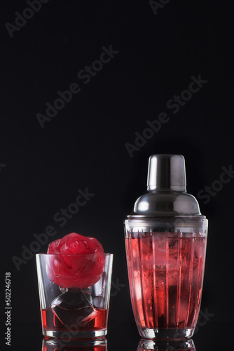 Red cocktail with ice in a glass and a shaker on a black background. Summer cold alcoholic soft drinks, drinks and cocktails.