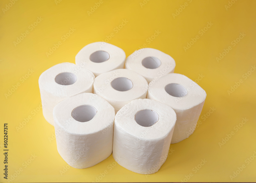On a yellow background, seven rolls of toilet paper stand side by side On a yellow background, seven rolls of toilet paper stand side by side