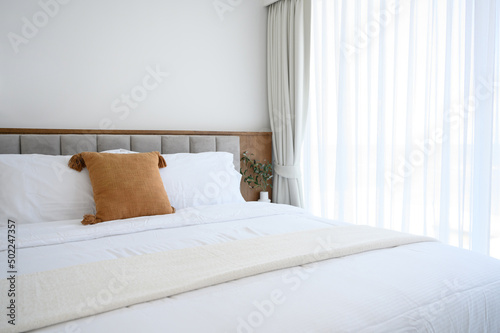Modern interior cozy bed near a window with white curtains in bedroom. pillows and white soft blanket for rest and sleep.