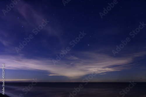 Starry night sky over calm sea beach.