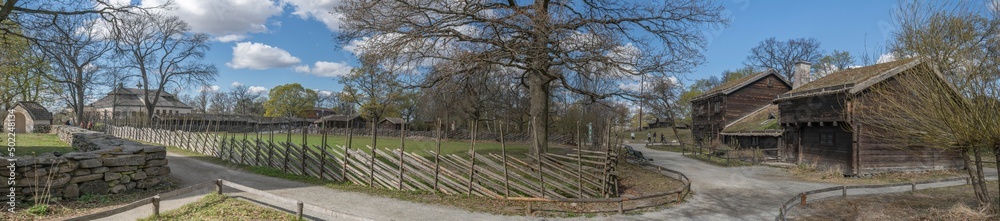 Historical buildings in a park, log houses with Birch-bark roof a sunny spring day in Stockholm