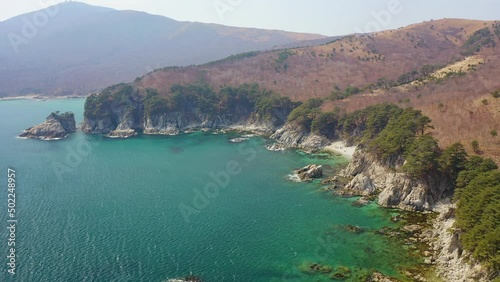 A beautiful rocky island and a cape in a beautiful bay covered with coniferous trees. Sea waves crash on the shore. Beautiful rocks are covered with pine trees. The concept of outdoor recreation photo