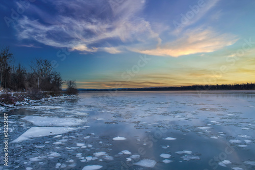 Beautiful sunset on river in winter with ice floes, clouds, nobody