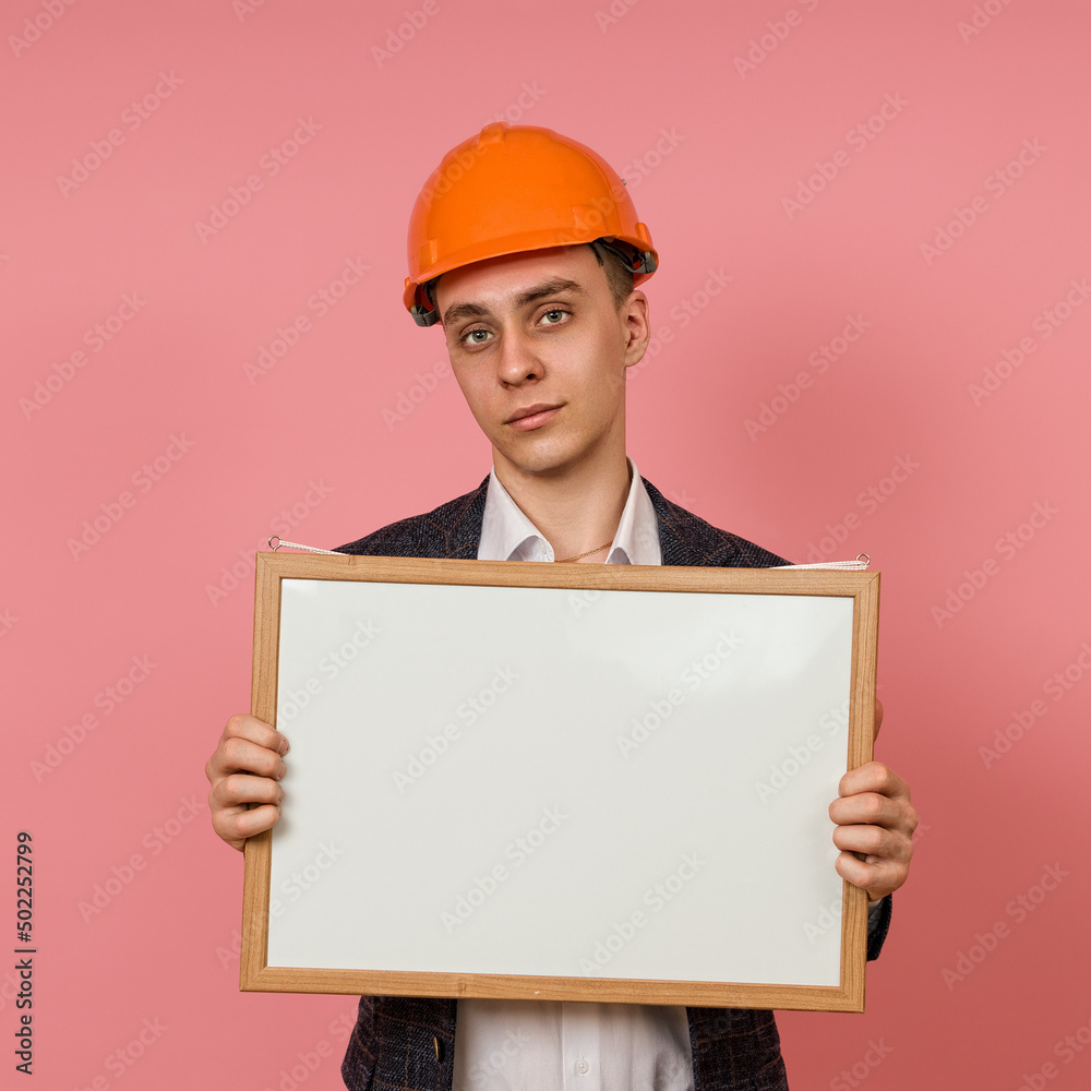 young engineer in a protective helmet and jacket with a white board in his hands on a pink background young engineer in a protective helmet and jacket with a white board in his hands on a pink background