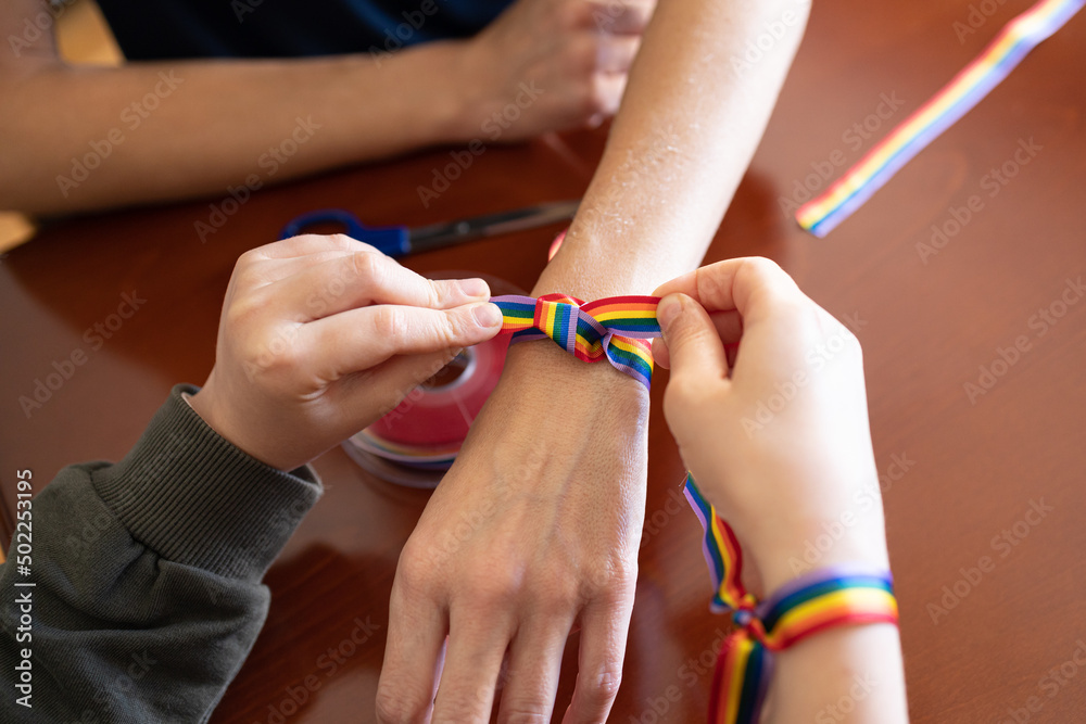 Young girl putting a LGBT rainbow bracelet on a woman's wrist