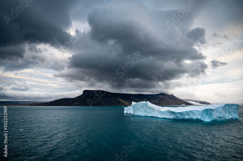 Tabular iceberg west of James Ross Island in Antarctica with J.R. Island in background with mystic cloudy sky.