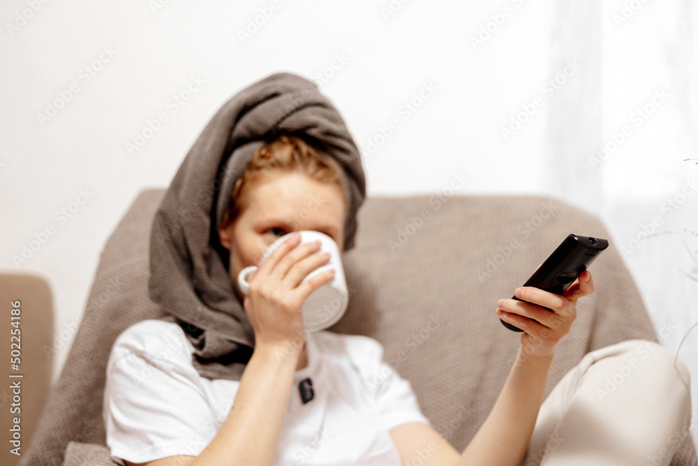 Young woman with casual clothes, towel on head drinking hot tea and resting, watching TV. Relax after taking shower. Self care, time for yourself. Relaxing at home. Young woman with casual clothes, towel on head drinking hot tea and resting, watching TV. Relax after taking shower. Self care, time for yourself. Relaxing at home.