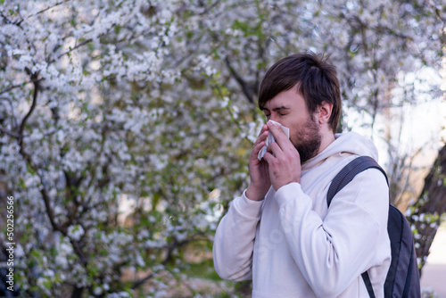 Man with nose wiper rubs nose with handkerchief near blooming tree seasonal allergy