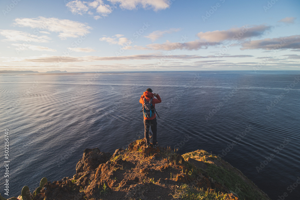 Passionate backpacker at 24 years old stands on the edge of a cliff in a place called Cristo Rei, Camara de Lomos, Madeira, belonging to Portugal. Sunrise on the Atlantic coast
