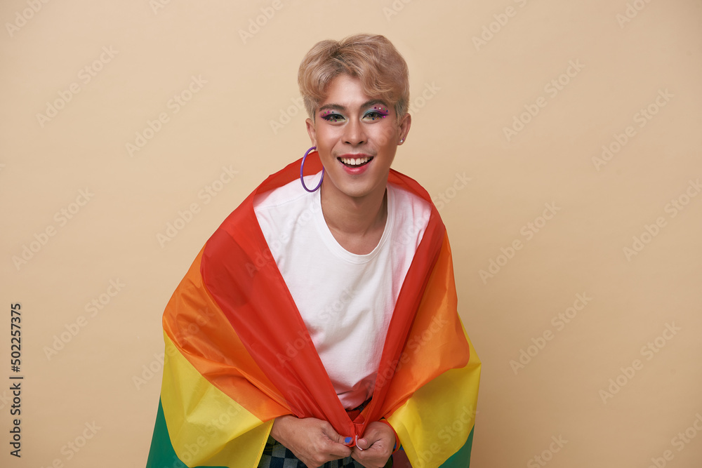Youth asian transgender LGBT with Rainbow flag on shoulder isolated over nude color background. gender expression pride and equality concept. Youth asian transgender LGBT with Rainbow flag on shoulder isolated over nude color background. gender expression pride and equality concept.