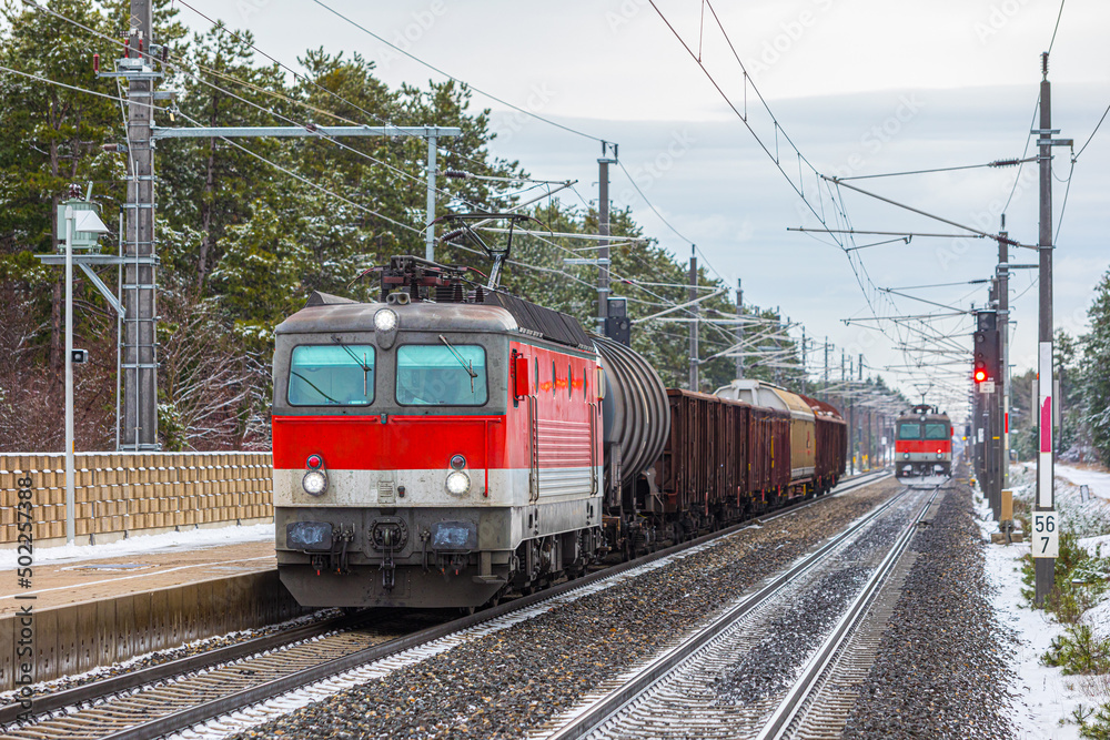 Two freight trains loaded with goods are moving along the tracks of the railway station. Winter photography. Freight railway transportation of goods.