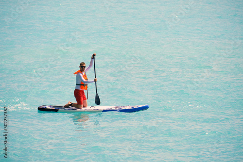 Young man dressed in swimsuit and lifevest paddling on stand up paddle board 