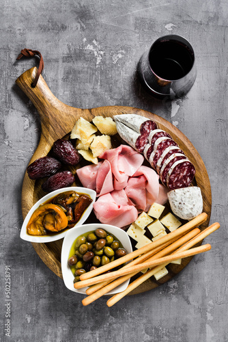 Italian snack and antipasti on a tray and red wine: prosciutto, salami, sun-dried tomatoes, olives, cheese, grissini and dates. Summer snack