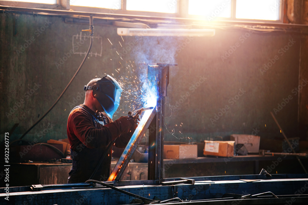 Factory worker in protective mask welding iron parts Factory worker in protective mask welding iron parts
