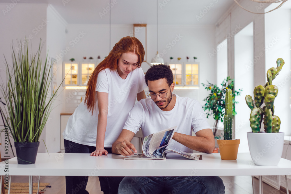 The couple reading a magazine together at the table. African American guy and red-haired girl. The couple reading a magazine together at the table. African American guy and red-haired girl.