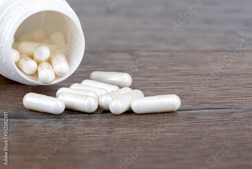 Close-up of Vitamin D pills and a bottle of capsules or medicines on a wooden background.