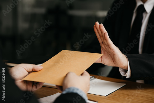 Business man raised her hand to deny accepting a bribe from a business partner, a brown envelope containing a large number of dollar bills as money for bribery, a corruption concept. photo