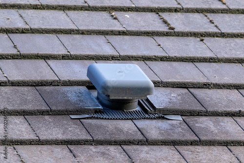A close up portrait of a roof vent on a slate roof on a house. This small chimney like object is used as a ventilation, to ventilate a house and regulate the air flow or air supply of a building.