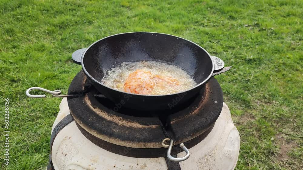 Cooking grilled chicken in a wok over an open fire. Girl cook puts food in boiling oil. 27 April 2022, Minsk, Belarus Cooking grilled chicken in a wok over an open fire. Girl cook puts food in boiling oil. 27 April 2022, Minsk, Belarus