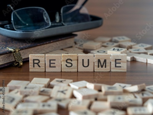resume word or concept represented by wooden letter tiles on a wooden table with glasses and a book