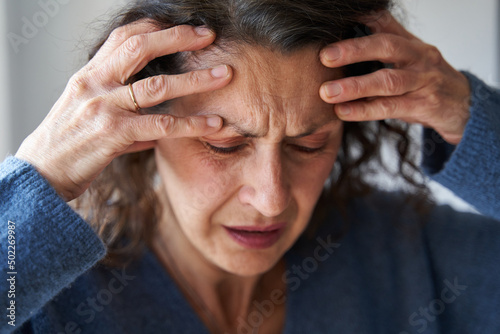 Mature woman with strong migraine holds head with ands