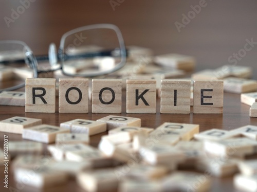 rookie word or concept represented by wooden letter tiles on a wooden table with glasses and a book photo