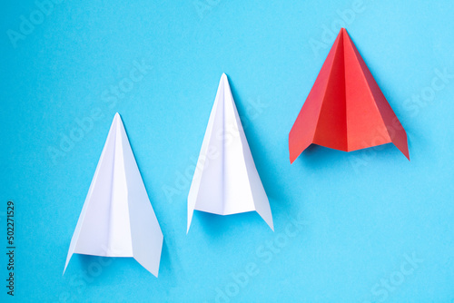 a red paper airplane and two white ones on a blue background. The concept of leadership, teamwork and courage. © Alena