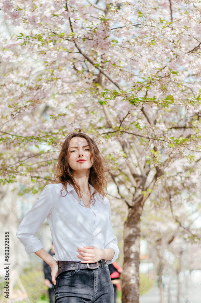 girl in a white shirt stands near the blossoming sakura in the spring girl in a white shirt stands near the blossoming sakura in the spring