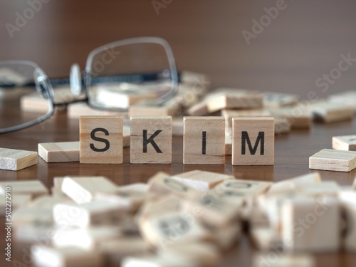 skim word or concept represented by wooden letter tiles on a wooden table with glasses and a book photo