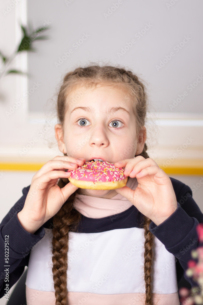 Little girl with braided hair biting into a pink frosted donut, expressing surprise in a home setting. Little girl with braided hair biting into a pink frosted donut, expressing surprise in a home setting.
