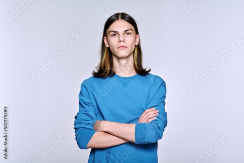Portrait of serious confident young male with folded hands looking at camera, light background