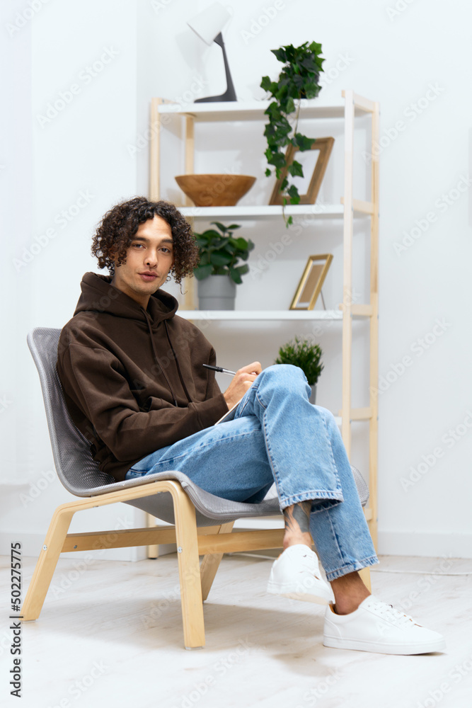 guy with curly hair writes in a notebook sitting on a chair in the room Lifestyle