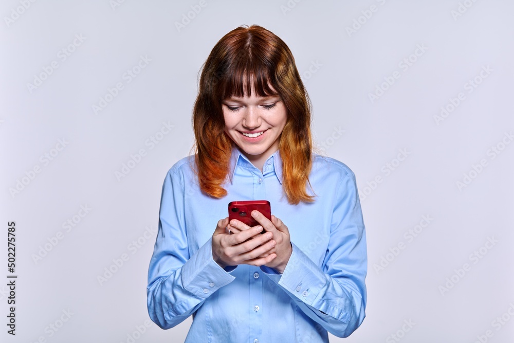 Smiling teenage female looking at smartphone screen, on light studio background Smiling teenage female looking at smartphone screen, on light studio background