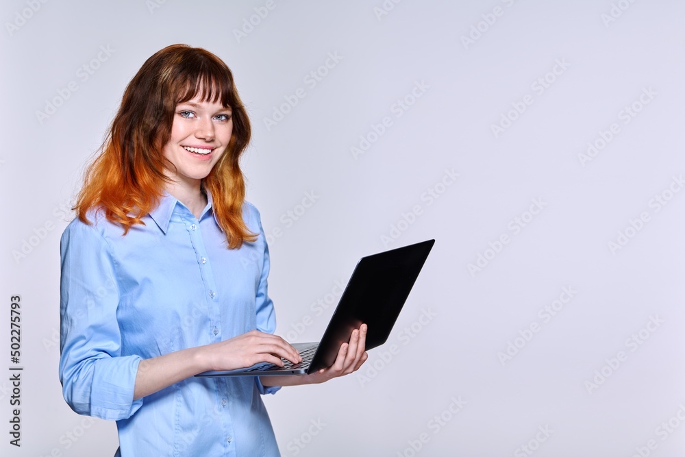 Beautiful teenage female with laptop looking at camera, light studio background Beautiful teenage female with laptop looking at camera, light studio background