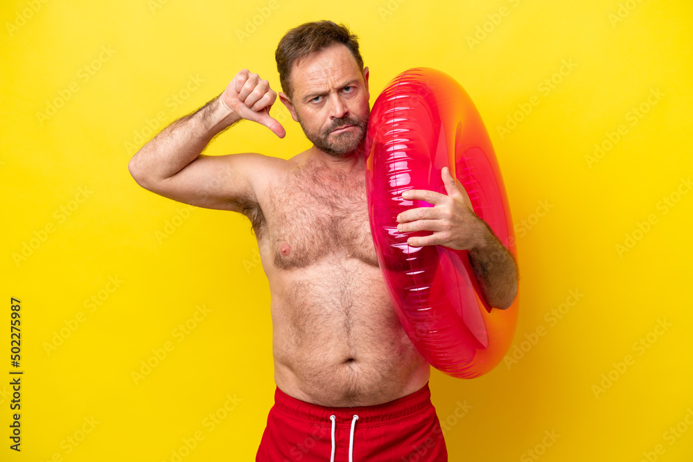 Middle age caucasian man holding inflatable donut isolated on yellow background showing thumb down with negative expression