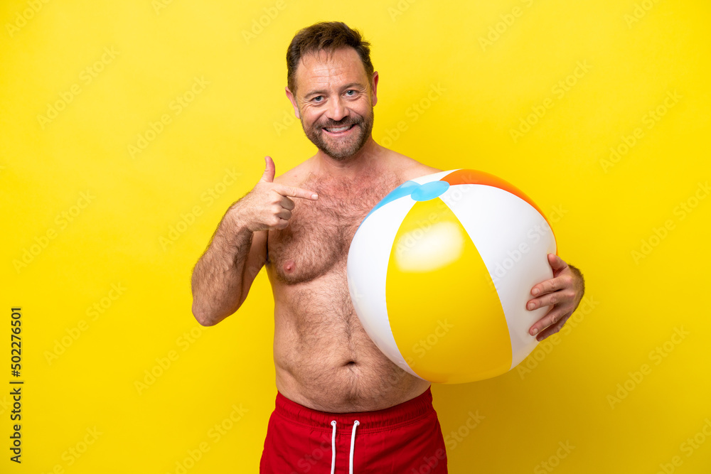 Middle age caucasian man holding beach ball isolated on yellow background pointing to the side to present a product Middle age caucasian man holding beach ball isolated on yellow background pointing to the side to present a product