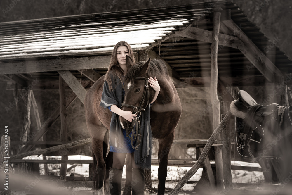 A girl in a blue dress hugs a horse against the backdrop of a snow-covered canopy in the forest, muted colors