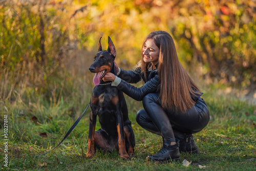 girl sitting near a doberman dog breed in nature
