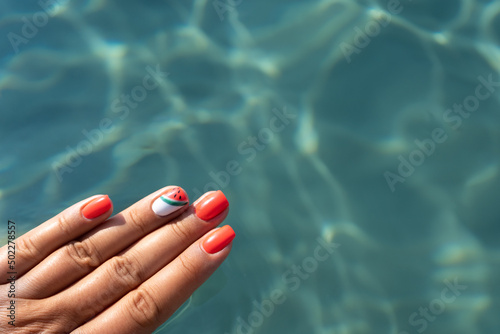 Woman hands with manicure with watermelon pattern on the background of a sea