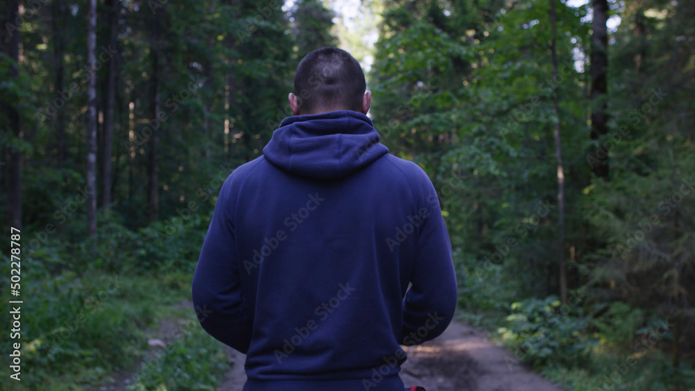 Fototapeta premium Person in a hood standing. Man in the hood in the woods. Sport in the forest on the nature