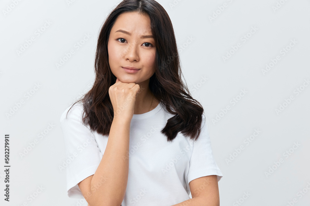 Pensive thoughtful upset cute Asian young female in white basic t-shirt can't make decision reclines on hand posing isolated on white studio background. The best offer for ad. People Lifestyle concept Pensive thoughtful upset cute Asian young female in white basic t-shirt can't make decision reclines on hand posing isolated on white studio background. The best offer for ad. People Lifestyle concept
