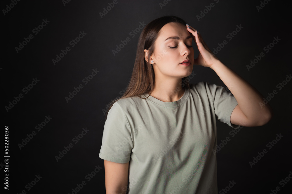 Headache. A young brunette in a T-shirt clutched her head with her hand, illness or fatigue. Portrait on a black background Headache. A young brunette in a T-shirt clutched her head with her hand, illness or fatigue. Portrait on a black background