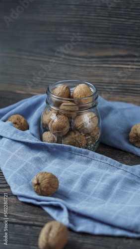 walnuts in a jar close-up on a wooden background. around the jar is a blue kitchen towel