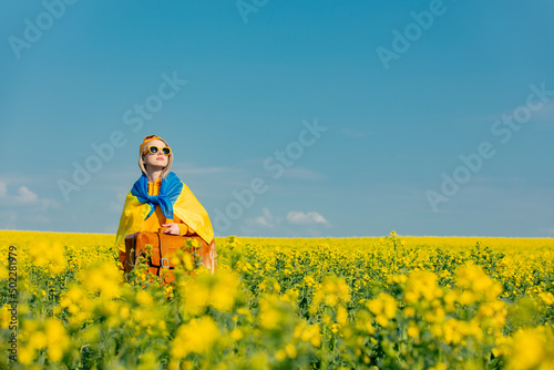 Ukrainian woman in yellow hoodie and ukraine flag with bag in rapeseed field