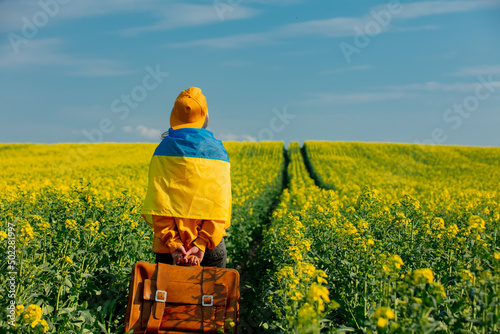Stampa su tela Ukrainian woman in yellow hoodie and ukraine flag with bag in rapeseed field