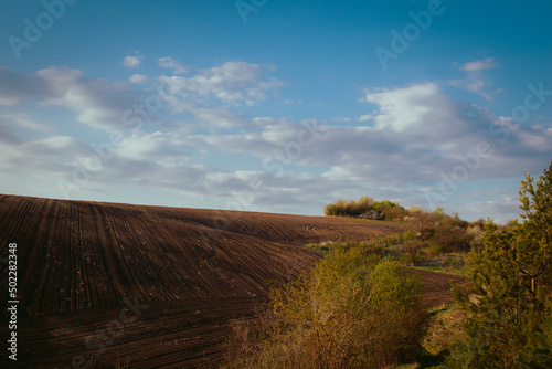Countryside panorama with arable land on hills with blue sky and white clouds. With copyspace for text