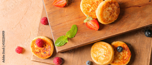 Boards with tasty cottage cheese pancakes and berries on color background