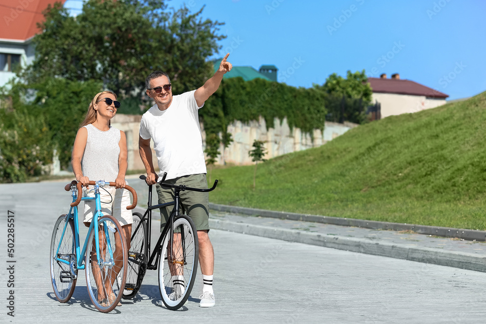 Mature couple with bicycles walking in city park on summer day Mature couple with bicycles walking in city park on summer day