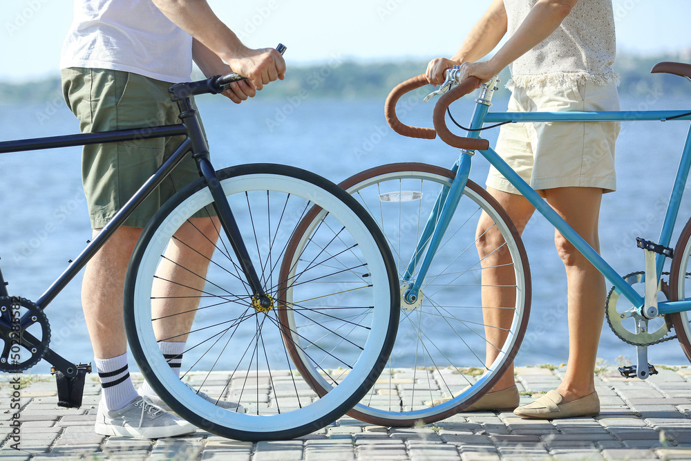 Obraz premium Mature couple with bicycles walking along river bank on summer day